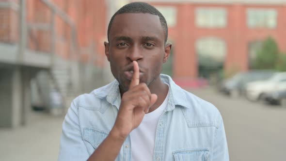Outdoor Portrait of African Man Showing Quiet Sign By Finger on Lips