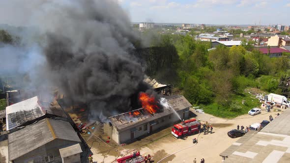 Aerial view of firefighters extinguishing ruined building on fire with collapsed roof and rising