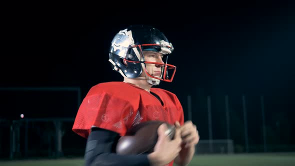 One American Football Player Walks on a Field, Holding a Ball, Side View