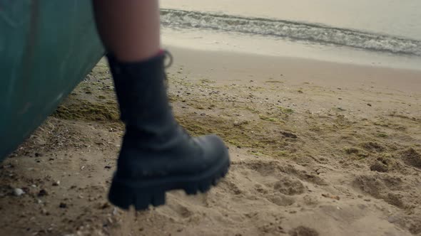 Woman Leg Wearing Black Boot Hanging From Old Boat Standing Sand Beach Close Up