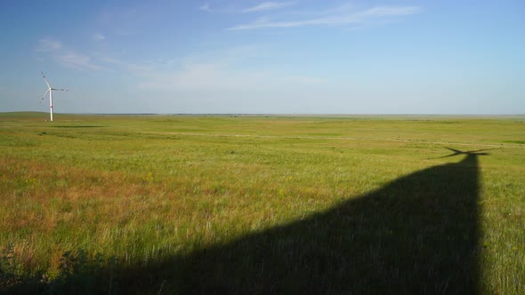 Shadow of Blades of a Large Wind Turbine in a Field with Green Grass