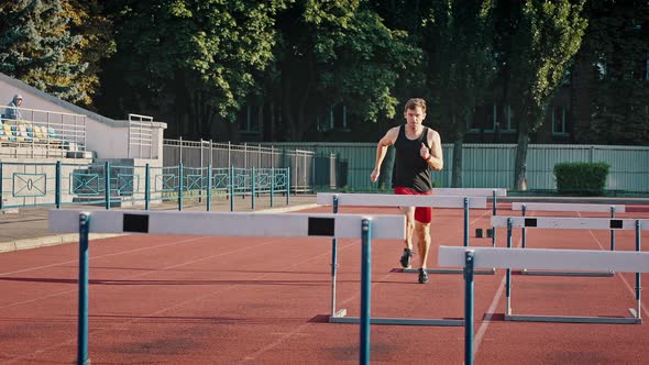 Active Guy Athlete in Sports Shorts and a Tshirt Runs a Distance Jumping Over Obstacles