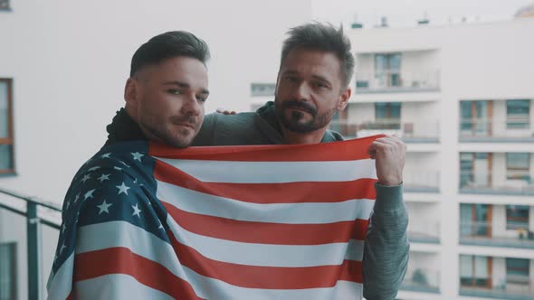 Young Handsome Gay Couple Standing on the Balcony Covered with USA Flag