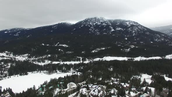 Drone in flight over winter village built for leisure in thick of rocky mountains