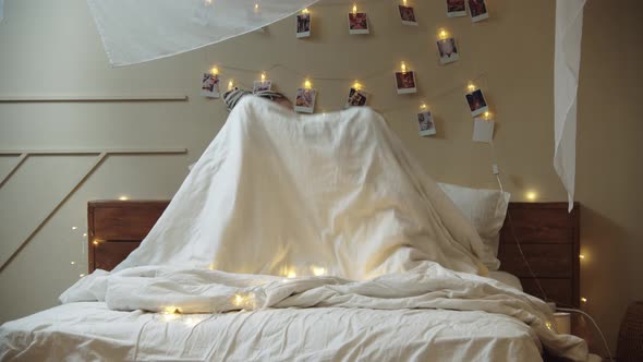 Two Young Women Lie on the Bed and Cover with a Blanket with Their Heads