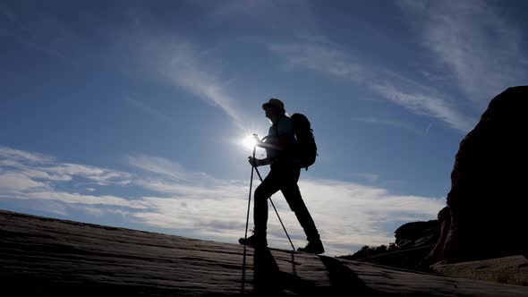 Silhouette Of Hiker With A Backpack Hiking Uphill On Background Of Sunset Rays