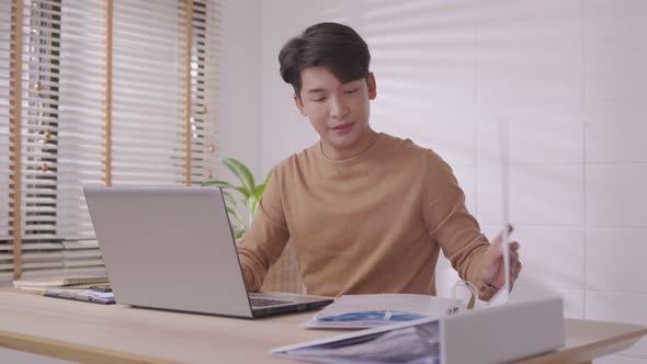 At home, an Asian businessman works on a desk with a laptop, searching for jobs and paperwork.