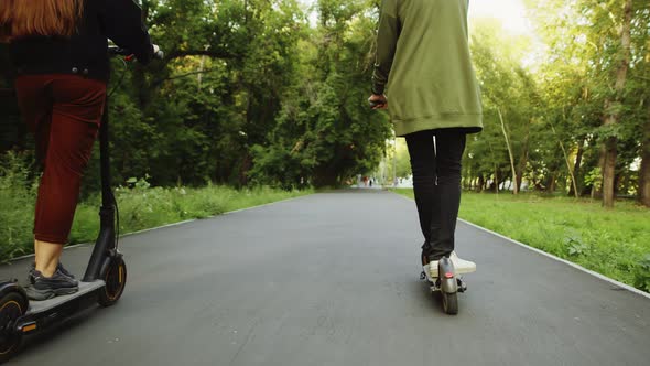 Couple Ride on Electric Scooters on Asphalt Path in Park Back View