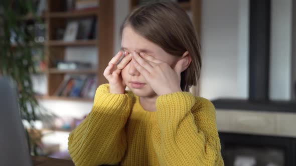 Tired girl rubbing eyes after learning at laptop