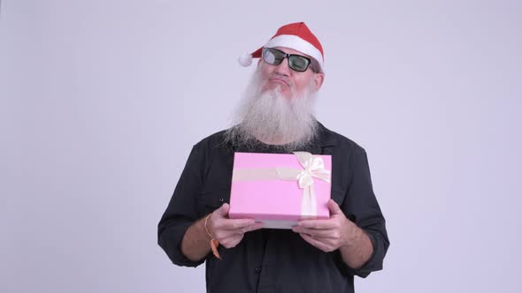Mature Bearded Hipster Man As Santa Claus Thinking While Holding Gift