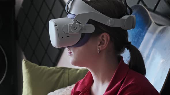 Young Woman in VR Helmet Sitting on Sofa and Communicating in Virtual World
