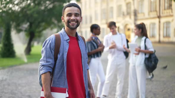 Smiling Handsome Middle Eastern Young University Student Posing at Campus with Blurred Multiethnic