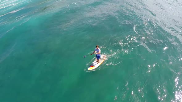 Aerial view of a man paddling while sup stand-up paddleboard surfing in Hawaii