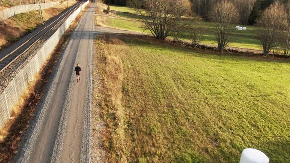 Man Running Down Countryside Dirt Road Next To Green Field Near Ostersund, Sweden. 4K Drone.
