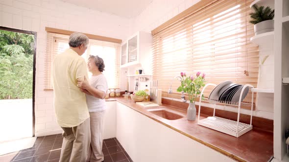 Asian elderly couple dancing together while listen to music in kitchen at home.