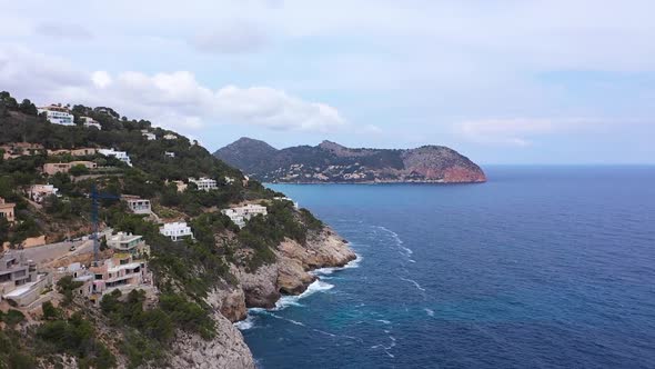 A cliff of Mallorca in which small houses were built. The sea laps against the coast. Filmed with a