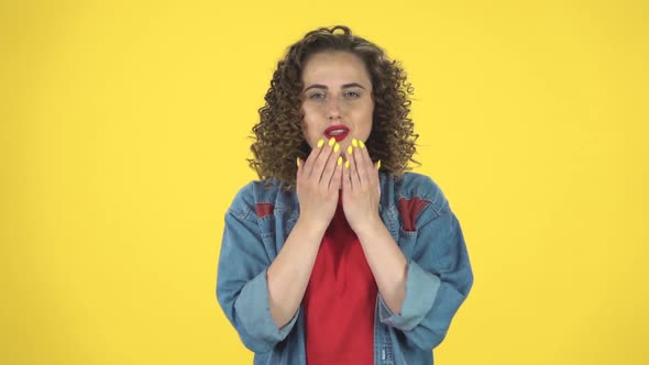 Cute Girl Smiles and Showing Heart with Fingers Then Blowing Kiss on Yellow Background, Slow Motion