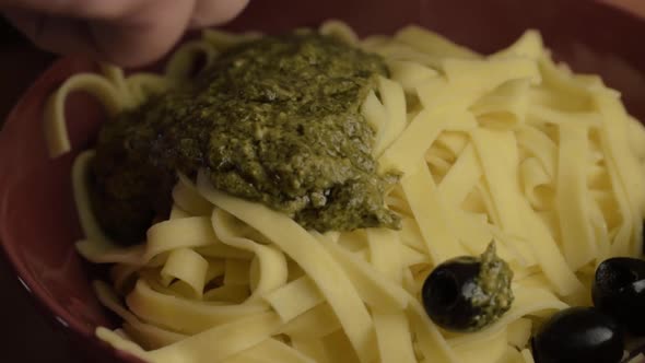 Serving tagliatelle pasta with green pesto sauce and black olives close up shot