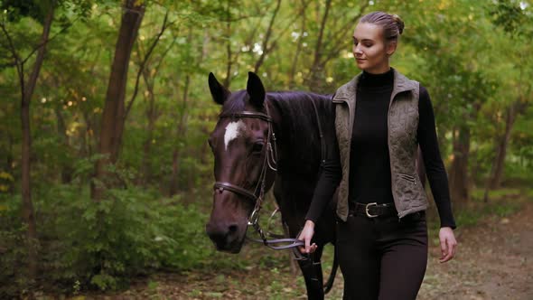 Attractive Female Jokey is Petting a Stunning Brown Horse with White Spot on Forehead While Walking