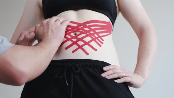 Therapist Placing Kinesiology Tape on Woman's Shoulder in Clinic