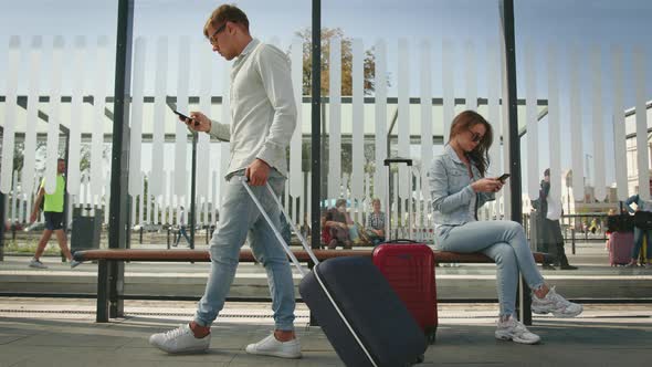 A Young Woman is Sitting at a Public Transport Stop and Texting on Her Smartphone