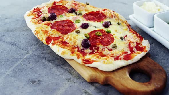 Baked pizza with olive and peperoni toppings served on chopping board
