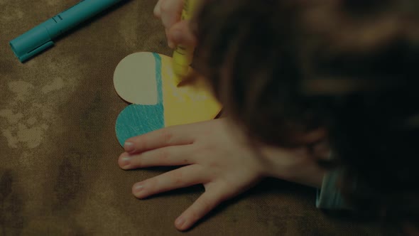 A child paints a heart in the colors of the flag of Ukraine, top view. color grading