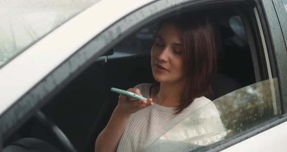 Happy Woman Sitting Inside Car Using a Smart Phone Voice Recognition Function Online Outdoors Speech