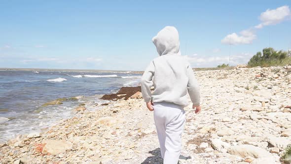 Small 4 Year Old Boy Walks on a Rocky Beach in Windy Weather