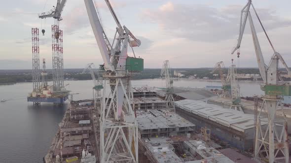 Construction Cranes At The Shipyard With Unfinished Cargo Ship