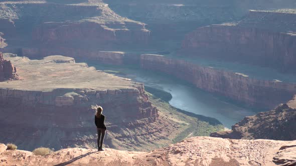 Slow motion shot of female tourist standing on cliff looking at Colorado River in Dead Horse Point S