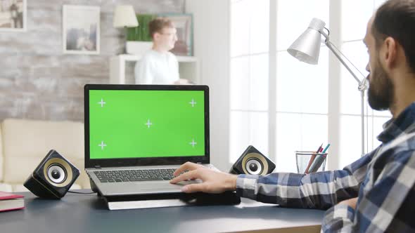 Young Man Looks at Laptop with Chroma Green Screen Mock-up