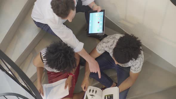 People sitting together in stairwell looking at digital tablet and reviewing documents