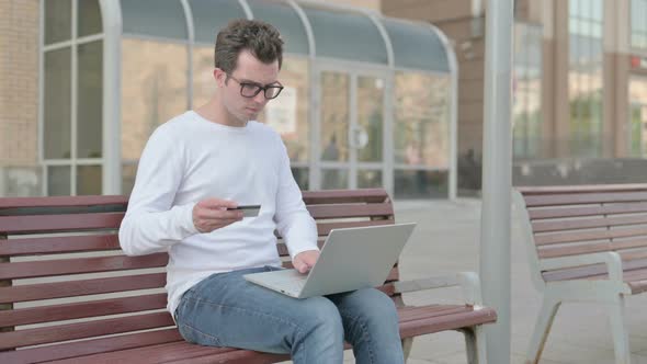 Excited Young Man Shopping Online with Laptop Outdoor