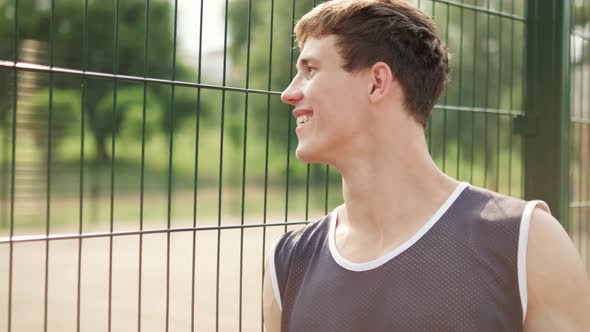 A smiling guy is watching people playing basketball