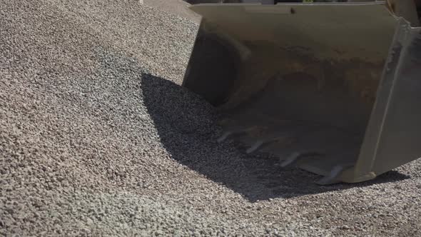 Side View of Tractor Bucket Downloading Crushed Stone Outdoors on Factory. Process of Material