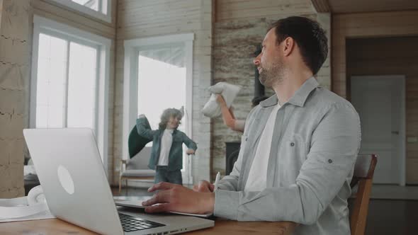 Man Put on Headphones Working at Home Because His Children Fighting with Pillows