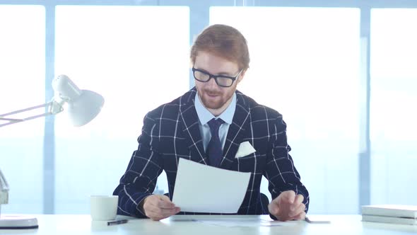 Happy Man Reading Papers at Work in Good Mood, Positive