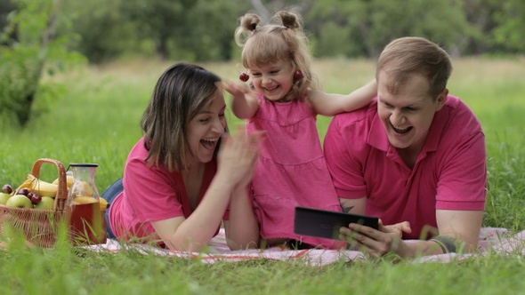 Family Weekend Picnic. Daughter Child Girl with Mother and Father Browsing on Internet on Tablet