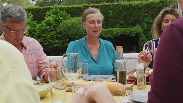 Animation of happy diverse female and male senior friends having lunch in garden, praying