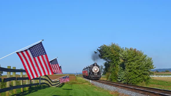 A View of a Line of Gently Waving American Flags on a Fence by Farmlands as a Steam Passenger Train