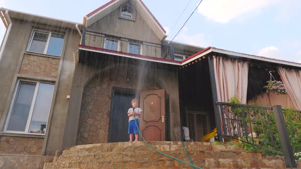 Games with water hose. Boy playing with water hose in the backyard of a country house in the summer