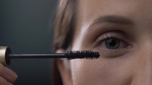 Close Up Shot of Young Woman Applying Mascara on Eyelashes Against Black Background