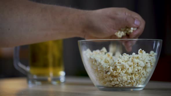 Man eating popcorn and drinking a beer while watching movie at home, close-up