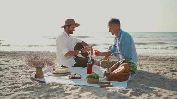 European Happy Gay Couple Drinking Wine and Enjoying Romantic Picnic at Beach