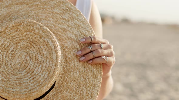 Close Up Woman Hands with Boho Gypsy Rings Holding Straw Trendy Hat. Girl Standing on Sandy Beach at