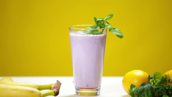 Closeup Purple Vitamin Smoothie with Mint and Lemon Juice Drops Falling in Slow Motion in Drink