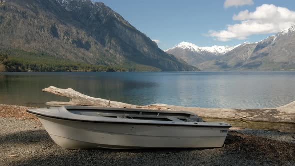 Panoramic view of the lake and mountains with a white boat and big log and blue sky panning from lef