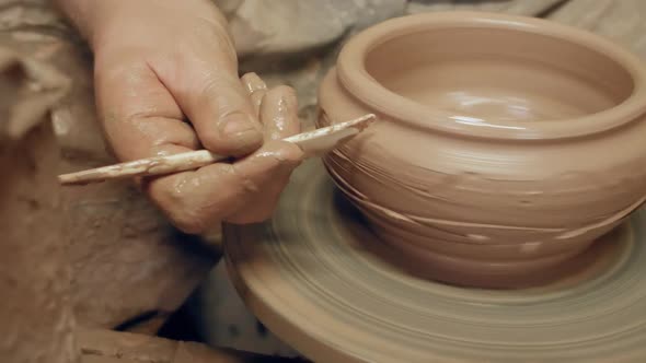 Apprentice decorating clay bowl with plastic knife on kick revolving pottery wheel