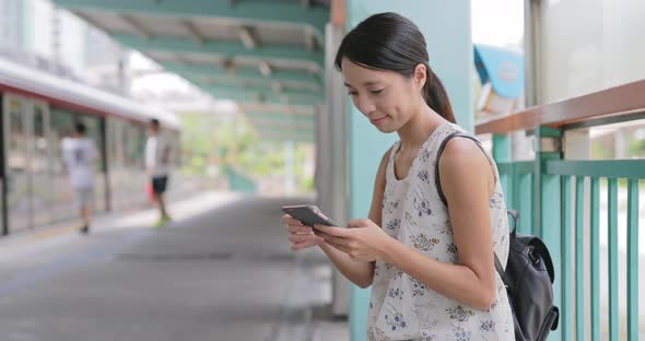 Woman playing on mobile phone and waiting for train 